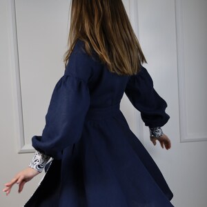 May include: A navy blue dress with long, puffed sleeves and a white and blue patterned trim. The dress has a flared skirt and is made of a soft, flowing fabric.