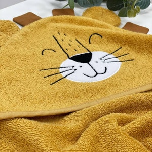 May include: A yellow hooded towel with a lion face embroidered on the hood. The lion has a black nose, white mouth, and black whiskers.