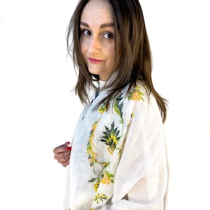 Puede incluir: Una blusa de lino blanca con dise&ntilde;os florales bordados en amarillo y verde. La blusa tiene mangas largas y un corte holgado.