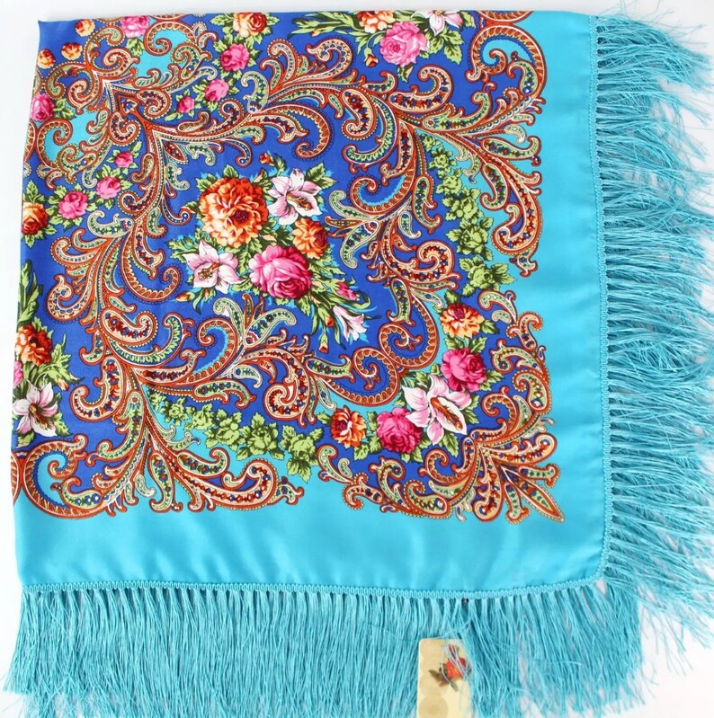 Pu&ograve; includere: Un foulard di seta blu turchese con un motivo floreale e paisley. Il foulard ha un bordo a frangia.