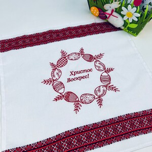 May include: White kitchen towel with a red embroidered border and a wreath of red Easter eggs with the text "Христос Воскрес!" in the center.