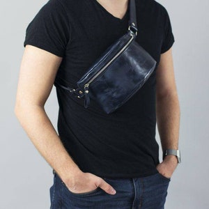 May include: A dark blue leather fanny pack with a silver zipper and strap. The bag is worn across the body.