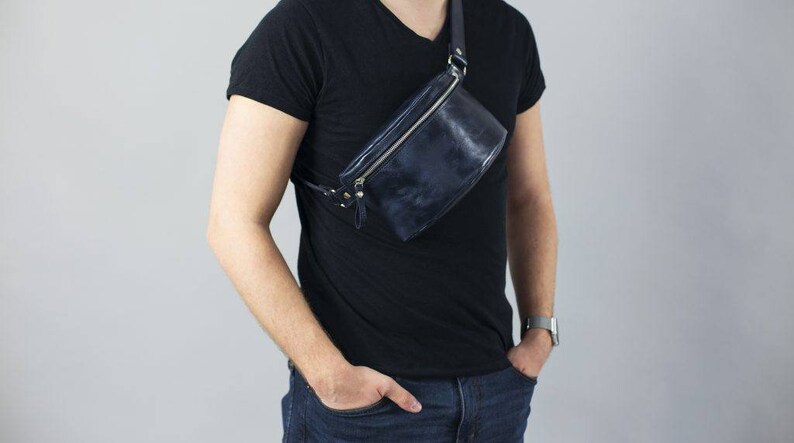 May include: A dark blue leather fanny pack with a silver zipper and strap. The bag is worn across the body.