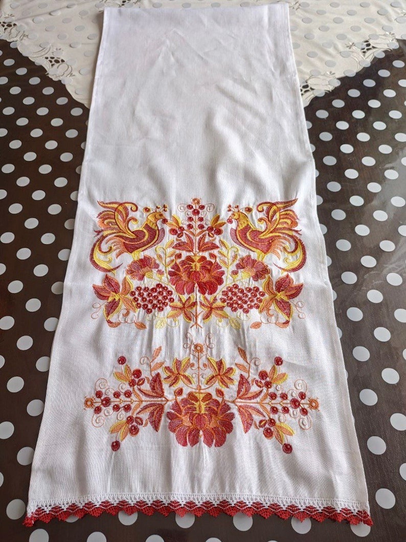 May include: White linen tea towel with red and yellow embroidered floral design and two birds. The towel has a red crocheted border.