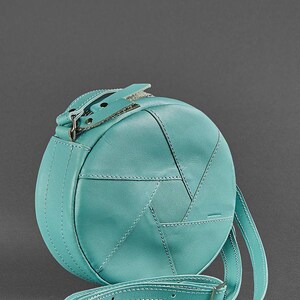 Puede incluir: Un bolso de hombro redondo de cuero azul turquesa con cierre de solapa y correa ajustable.