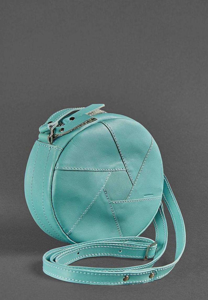 Puede incluir: Un bolso de hombro redondo de cuero azul turquesa con cierre de solapa y correa ajustable.