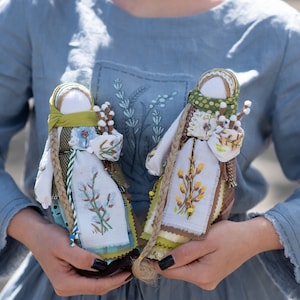 Puede incluir: Dos mu&ntilde;ecas de tela hechas a mano con detalles bordados. Las mu&ntilde;ecas est&aacute;n vestidas con tela blanca con detalles verdes y marrones. Sostienen ramitas de sauce.