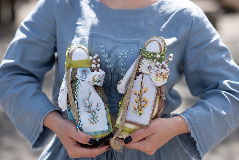 Puede incluir: Dos mu&ntilde;ecas de tela hechas a mano con detalles bordados. Las mu&ntilde;ecas est&aacute;n vestidas con tela blanca con detalles verdes y marrones. Sostienen ramitas de sauce.