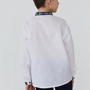 May include: A white long-sleeved shirt with a colorful embroidered trim around the collar. The shirt is made of a lightweight fabric and has a relaxed fit.