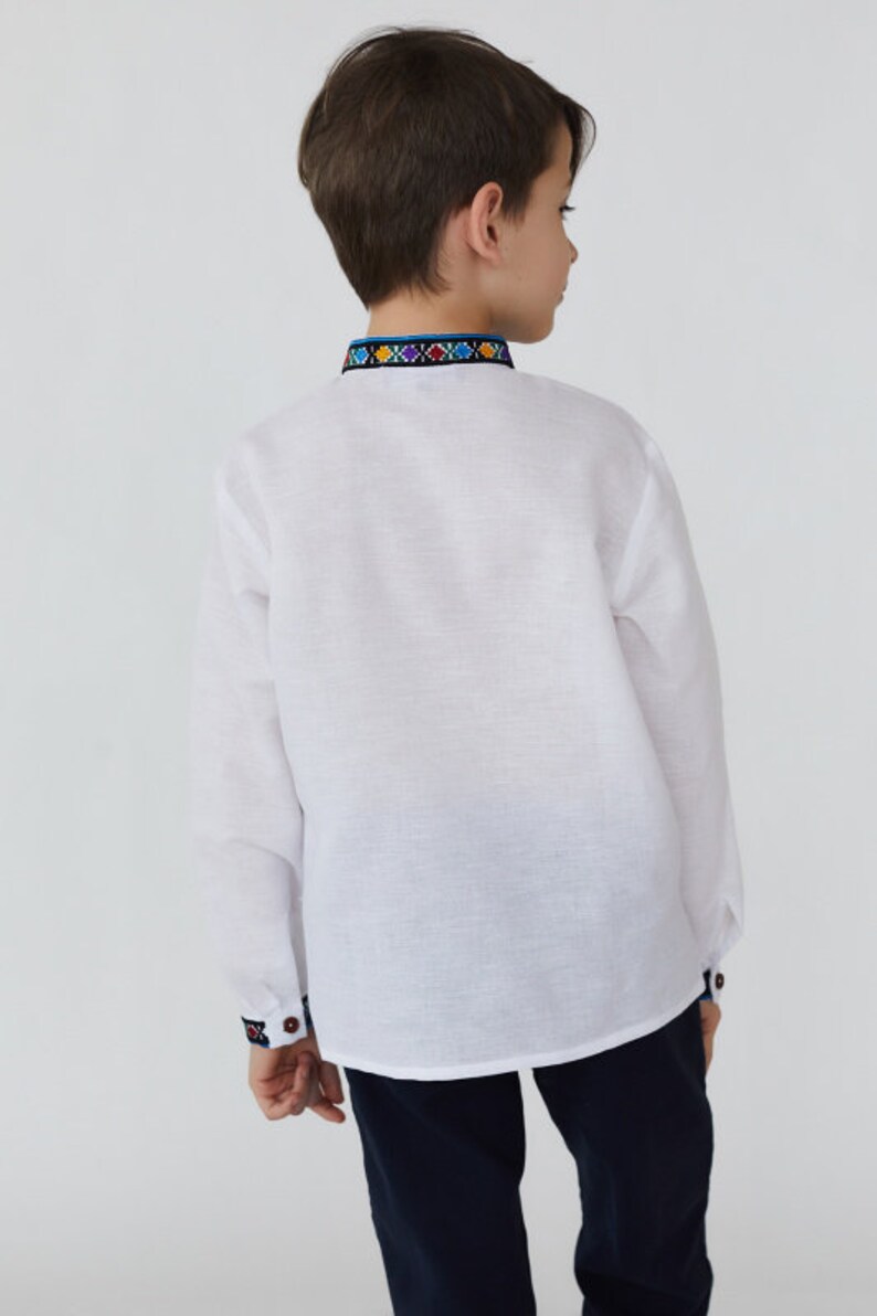May include: A white long-sleeved shirt with a colorful embroidered trim around the collar. The shirt is made of a lightweight fabric and has a relaxed fit.