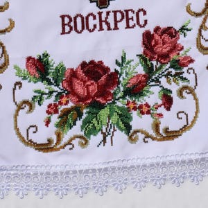 K&ouml;nnte beinhalten: Wei&szlig;es besticktes Tuch mit dem Wort "BOCKPEC" in Rot &uuml;ber einem floralen Design. Das Design umfasst rote Rosen, gr&uuml;ne Bl&auml;tter und goldene Filigranakzente. Der untere Rand hat eine wei&szlig;e Spitzentrim.