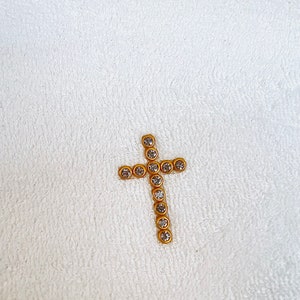 May include: A gold cross with clear rhinestones on a white towel.