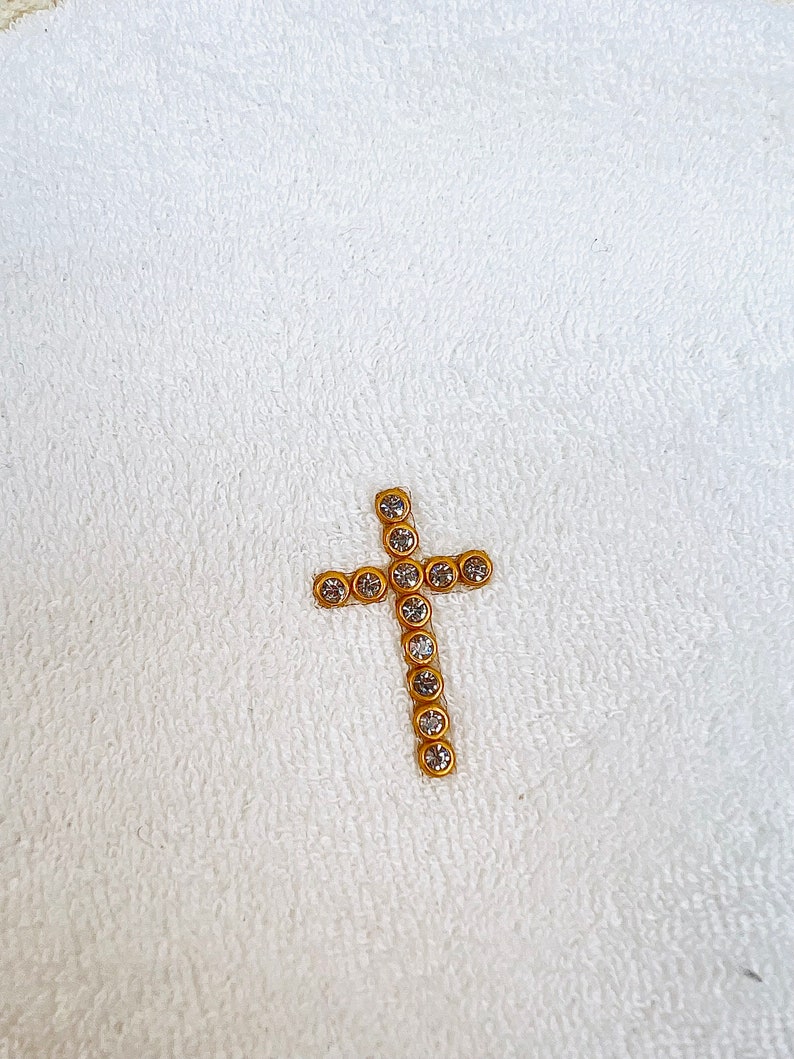 May include: A gold cross with clear rhinestones on a white towel.