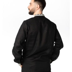 May include: Black long-sleeve shirt with a mandarin collar and decorative trim on the collar and cuffs. The shirt is made of a lightweight fabric and has a relaxed fit. The model is wearing black pants.
