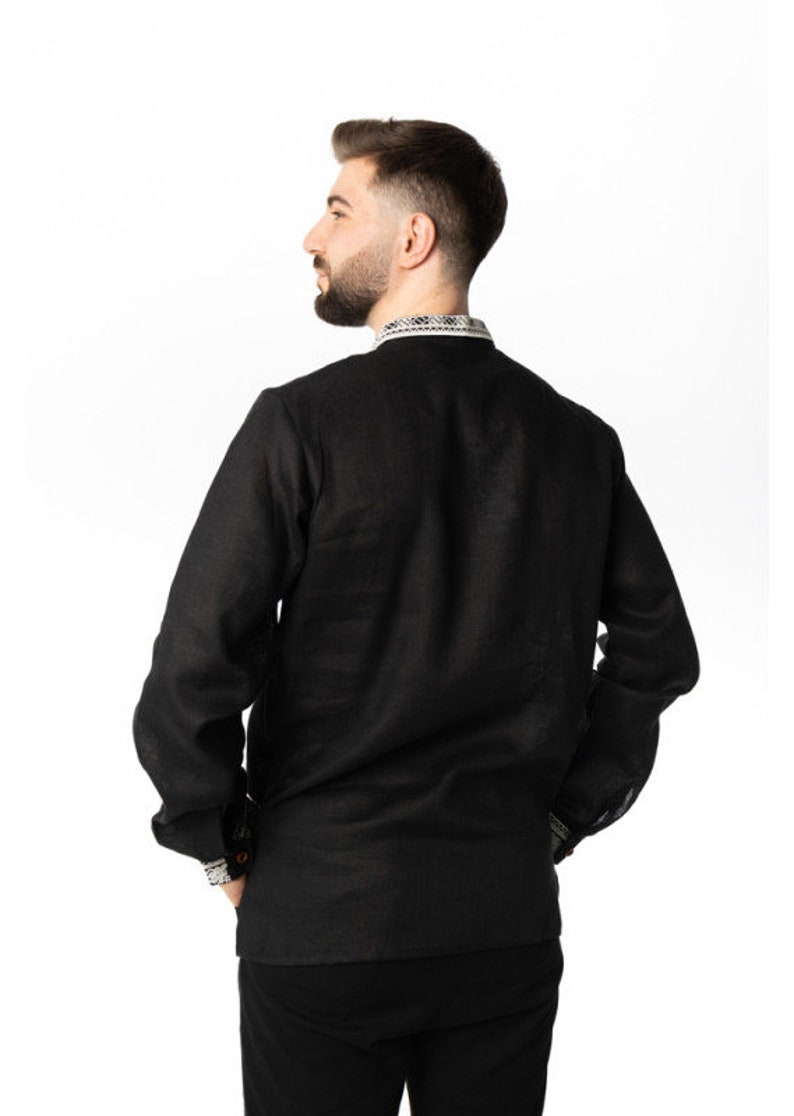 May include: Black long-sleeve shirt with a mandarin collar and decorative trim on the collar and cuffs. The shirt is made of a lightweight fabric and has a relaxed fit. The model is wearing black pants.