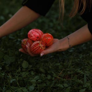 K&ouml;nnte beinhalten: Eine Hand h&auml;lt eine Sammlung von rot und orange dekorierten Ostereiern.