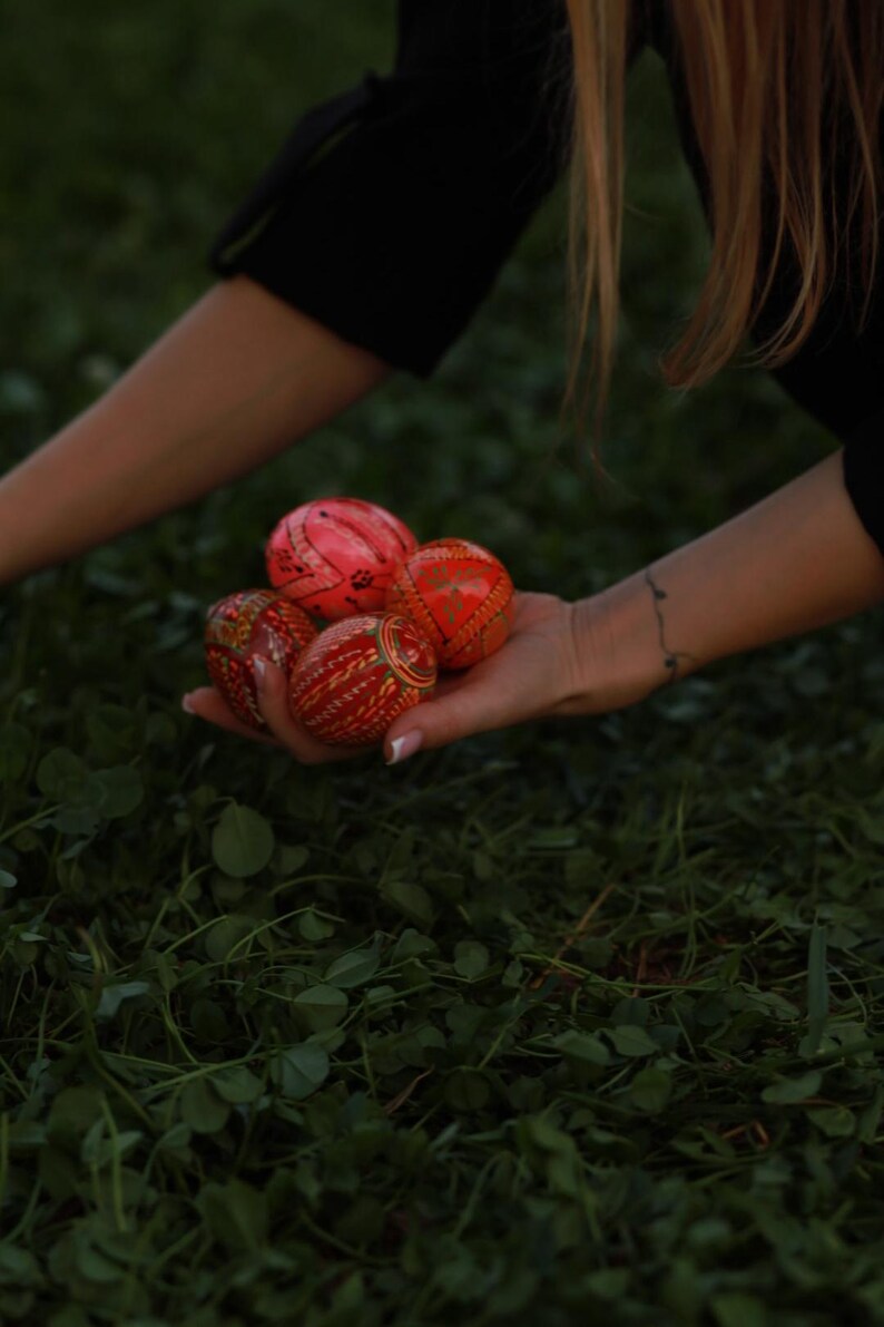 K&ouml;nnte beinhalten: Eine Hand h&auml;lt eine Sammlung von rot und orange dekorierten Ostereiern.