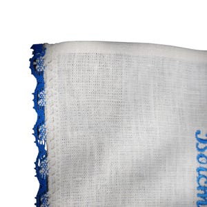 Puede incluir: Tela blanca con ribete de encaje azul. La tela tiene una textura tejida. El ribete de encaje est&aacute; en el lado izquierdo de la imagen. La tela tiene un dise&ntilde;o bordado azul en el lado derecho de la imagen.