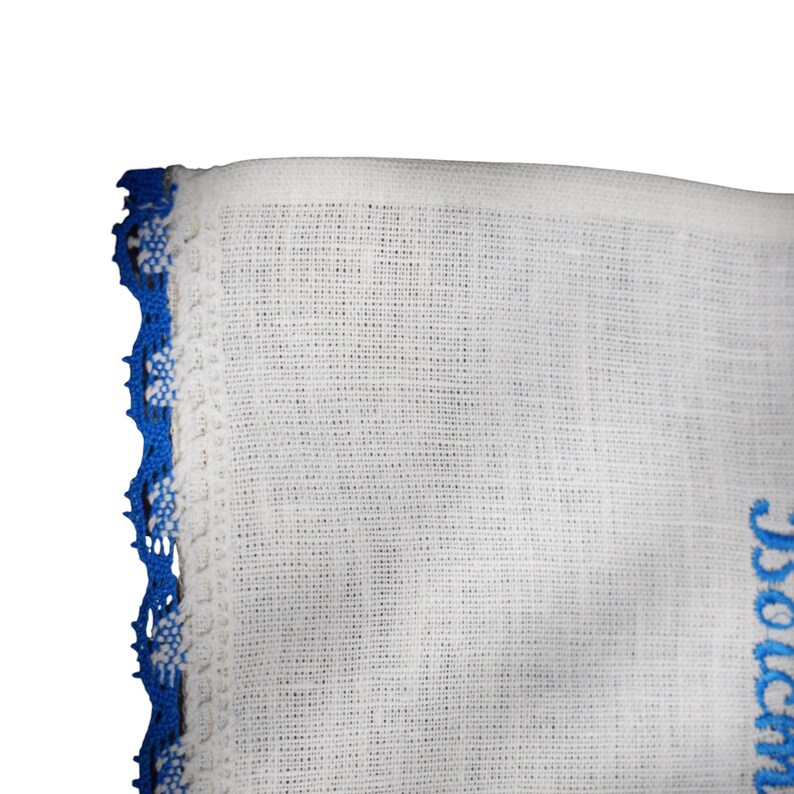 Puede incluir: Tela blanca con ribete de encaje azul. La tela tiene una textura tejida. El ribete de encaje est&aacute; en el lado izquierdo de la imagen. La tela tiene un dise&ntilde;o bordado azul en el lado derecho de la imagen.