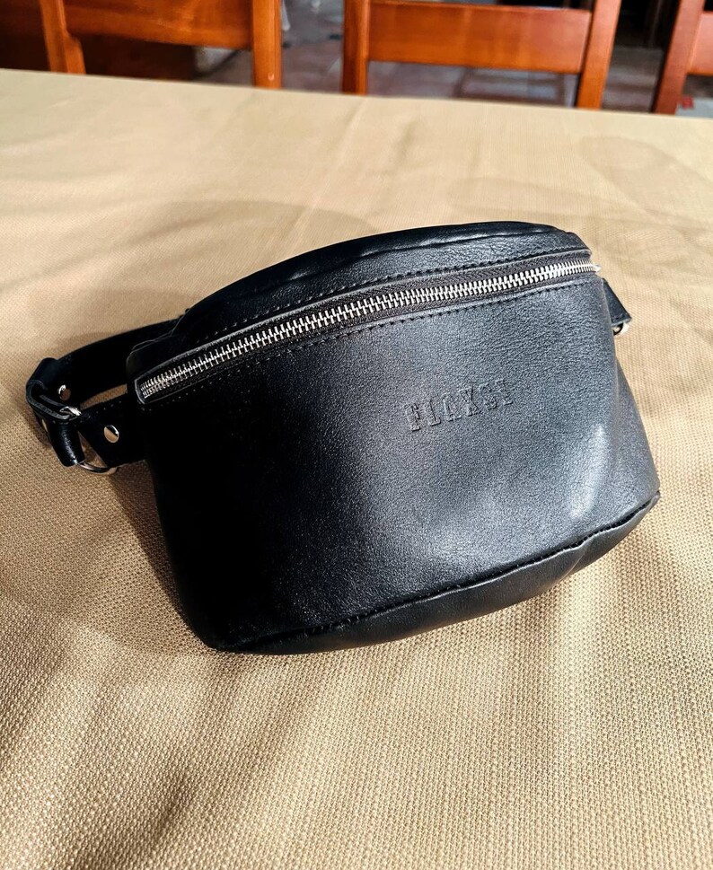 May include: A black leather fanny pack with a silver zipper and the word "BLACK" embossed on the front.