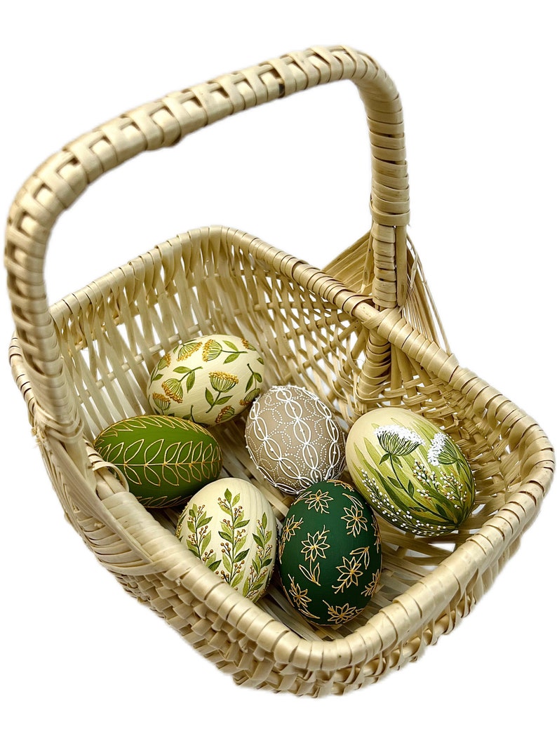 May include: A wicker basket filled with six hand-painted Easter eggs. The eggs are decorated with green and gold floral patterns.