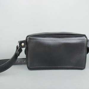 May include: A black leather crossbody bag with a long adjustable strap. The bag has a rectangular shape and a flap closure.