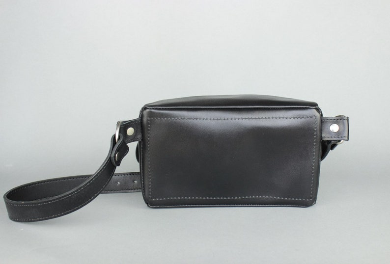 May include: A black leather crossbody bag with a long adjustable strap. The bag has a rectangular shape and a flap closure.