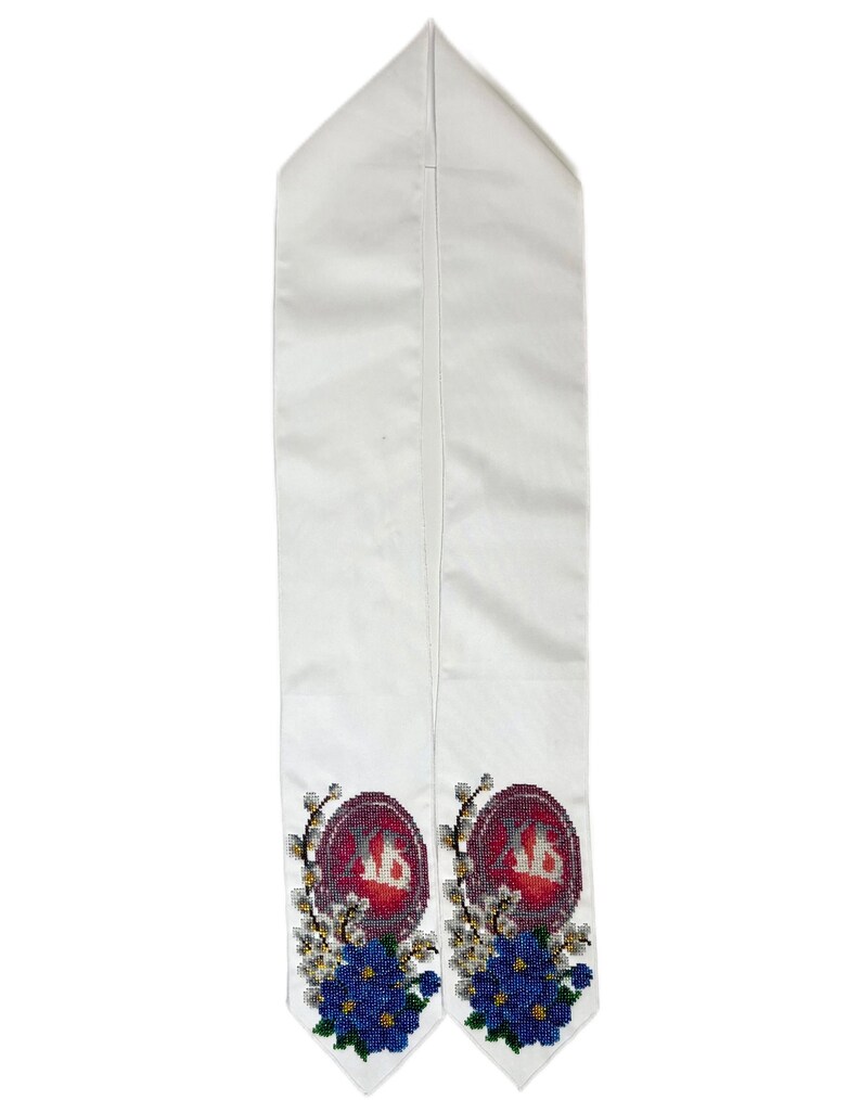 May include: White graduation stole with embroidered details. Features a maroon emblem with white lettering, surrounded by blue and white floral embroidery. The stole is made of a smooth, satin-like material.