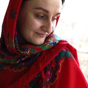 Puede incluir: Una mujer con un pa&ntilde;uelo rojo en la cabeza con un estampado floral colorido. El pa&ntilde;uelo est&aacute; atado alrededor de su cabeza y cubre su cabello. Ella est&aacute; mirando hacia abajo y sonriendo.