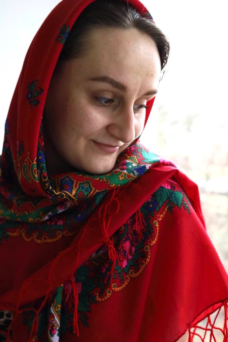 Puede incluir: Una mujer con un pa&ntilde;uelo rojo en la cabeza con un estampado floral colorido. El pa&ntilde;uelo est&aacute; atado alrededor de su cabeza y cubre su cabello. Ella est&aacute; mirando hacia abajo y sonriendo.