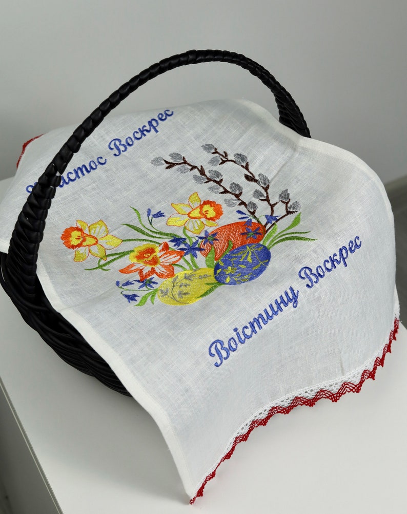 Puede incluir: Forro de cesta de Pascua de lino blanco con ribete de encaje rojo. El forro presenta flores bordadas, huevos y el texto "Христос Воскрес" y "Воистину Воскрес".