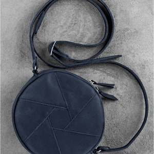 Puede incluir: Un bolso de hombro redondo de cuero azul oscuro con un patr&oacute;n geom&eacute;trico. El bolso tiene una correa larga ajustable y un cierre de cremallera.
