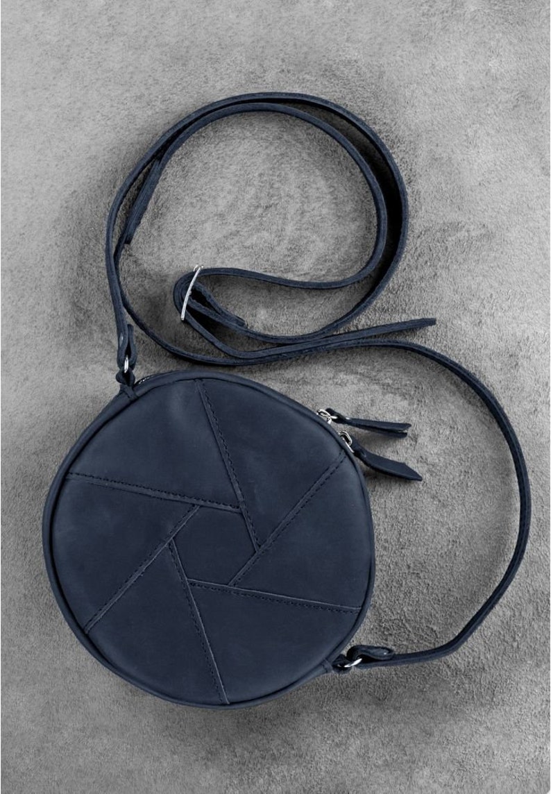 Puede incluir: Un bolso de hombro redondo de cuero azul oscuro con un patr&oacute;n geom&eacute;trico. El bolso tiene una correa larga ajustable y un cierre de cremallera.