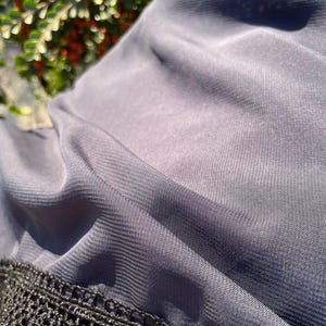 May include: A close-up of a dark gray sheer fabric with a black crocheted trim. The fabric is soft and flowing, with a subtle sheen.