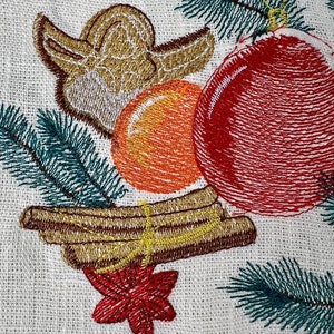 May include: Embroidered Christmas design featuring a red ornament, orange sphere, and gold angel. Green pine needles and cinnamon sticks with a red star are also included. The design is on a white fabric background.