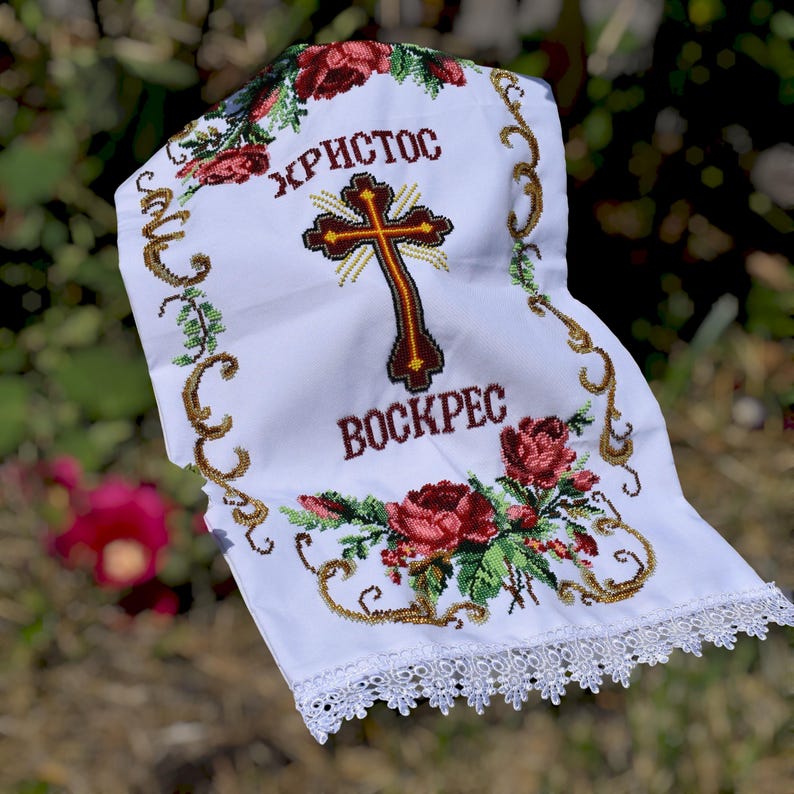 K&ouml;nnte beinhalten: Wei&szlig;es besticktes Tuch mit Kreuz- und Blumenmuster. Das Tuch tr&auml;gt die Worte "ХРИСТОС" und "ВОСКРЕС" in roter und brauner Farbe. Die R&auml;nder sind mit Spitze und goldfarbener Stickerei verziert.