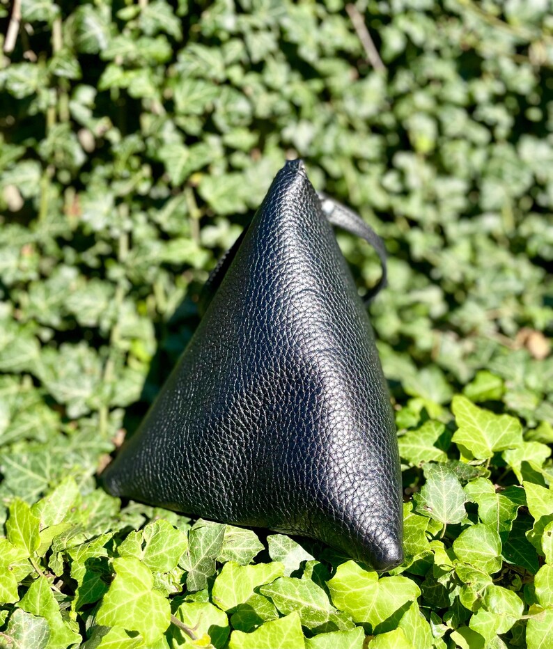 May include: A black leather triangular-shaped bag with a textured surface.