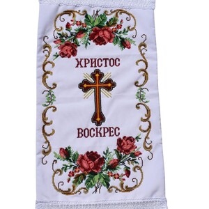 K&ouml;nnte beinhalten: Wei&szlig;es besticktes Tuch mit den Worten "ХРИСТОС ВОСКРЕС" und einem Kreuz in der Mitte. Das Design umfasst rote Rosen, gr&uuml;ne Bl&auml;tter und goldfarbene Ranken. Die R&auml;nder sind mit wei&szlig;er Spitze verziert.