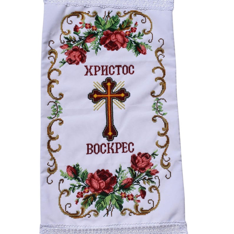 K&ouml;nnte beinhalten: Wei&szlig;es besticktes Tuch mit den Worten "ХРИСТОС ВОСКРЕС" und einem Kreuz in der Mitte. Das Design umfasst rote Rosen, gr&uuml;ne Bl&auml;tter und goldfarbene Ranken. Die R&auml;nder sind mit wei&szlig;er Spitze verziert.