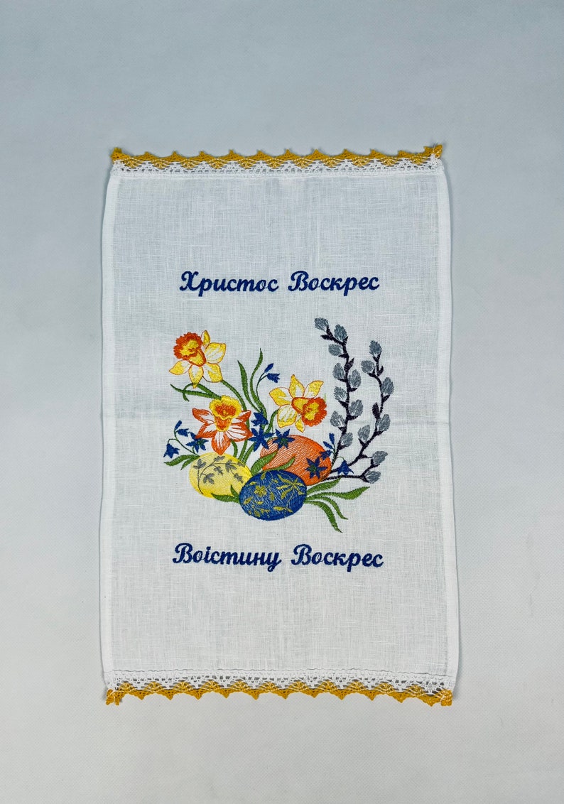 Puede incluir: Toalla de t&eacute; de lino blanco con narcisos amarillos, campanillas azules y ramas de sauce bordadas. El texto "Христос Воскрес" y "Воистину Воскрес" est&aacute; bordado en hilo azul.