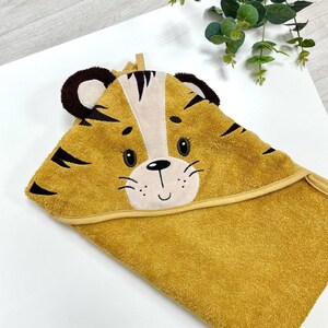 May include: A yellow hooded towel with a tiger face embroidered on the hood. The tiger has black stripes, brown ears, and a smiling face.