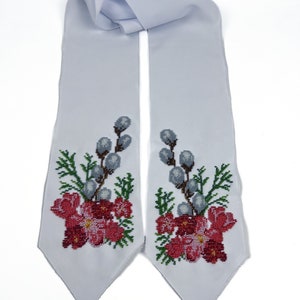 May include: A white satin sash with embroidered floral designs in shades of red, green, and white. The design features delicate flowers and willow branches.