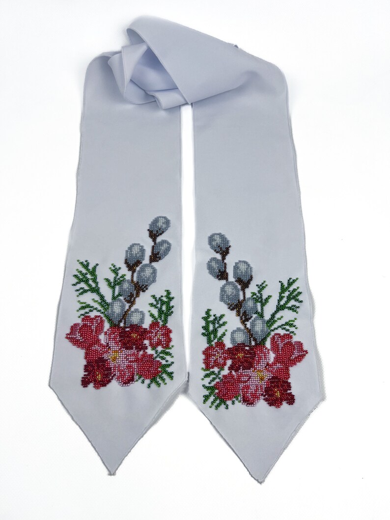 May include: A white satin sash with embroidered floral designs in shades of red, green, and white. The design features delicate flowers and willow branches.