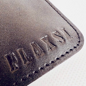 K&ouml;nnte beinhalten: Nahaufnahme eines schwarzen Lederportemonnaies mit dem Wort "PLAYFUL" gepr&auml;gt im Leder.
