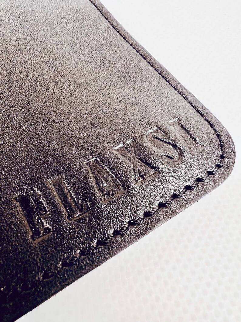 K&ouml;nnte beinhalten: Nahaufnahme eines schwarzen Lederportemonnaies mit dem Wort "PLAYFUL" gepr&auml;gt im Leder.