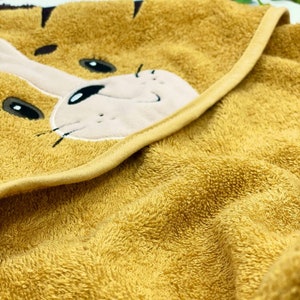 May include: A yellow hooded towel with a cute embroidered tiger face. The towel is made of soft, absorbent terry cloth.