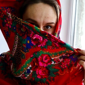 Puede incluir: Una mujer con un pa&ntilde;uelo rojo con estampado floral. El pa&ntilde;uelo cubre la mayor parte de su rostro, pero se puede ver un ojo.