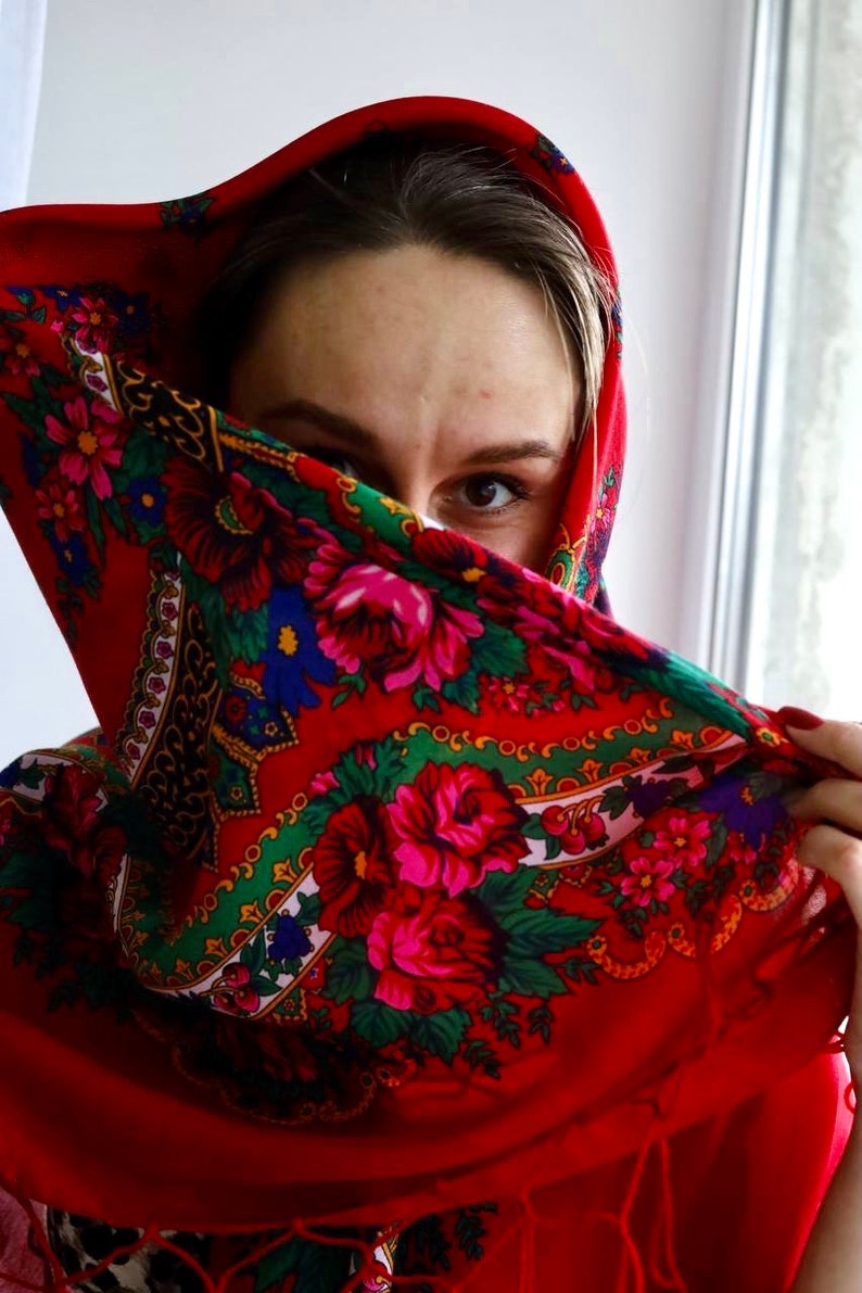 Puede incluir: Una mujer con un pa&ntilde;uelo rojo con estampado floral. El pa&ntilde;uelo cubre la mayor parte de su rostro, pero se puede ver un ojo.