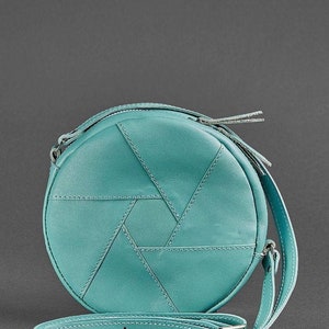 Puede incluir: Un bolso de hombro redondo de cuero azul turquesa con un patr&oacute;n geom&eacute;trico y una cremallera plateada. El bolso tiene una correa larga ajustable.