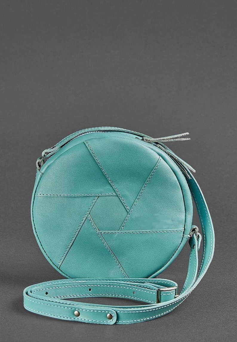 Puede incluir: Un bolso de hombro redondo de cuero azul turquesa con un patr&oacute;n geom&eacute;trico y una cremallera plateada. El bolso tiene una correa larga ajustable.